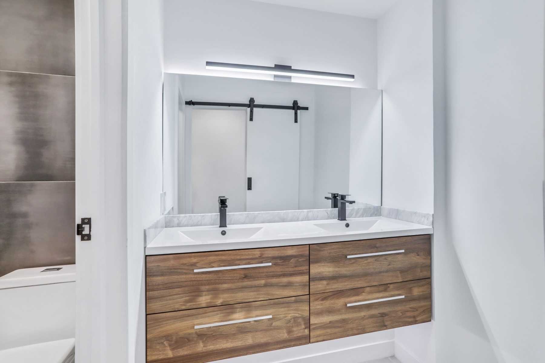 Double wood vanity with black fixtures and illuminated mirrors